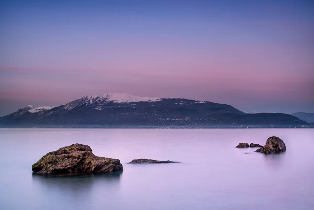 Foto del lago di Garda visto dalla riva, sullo sfondo il monte Baldo innevato e la costa veronese